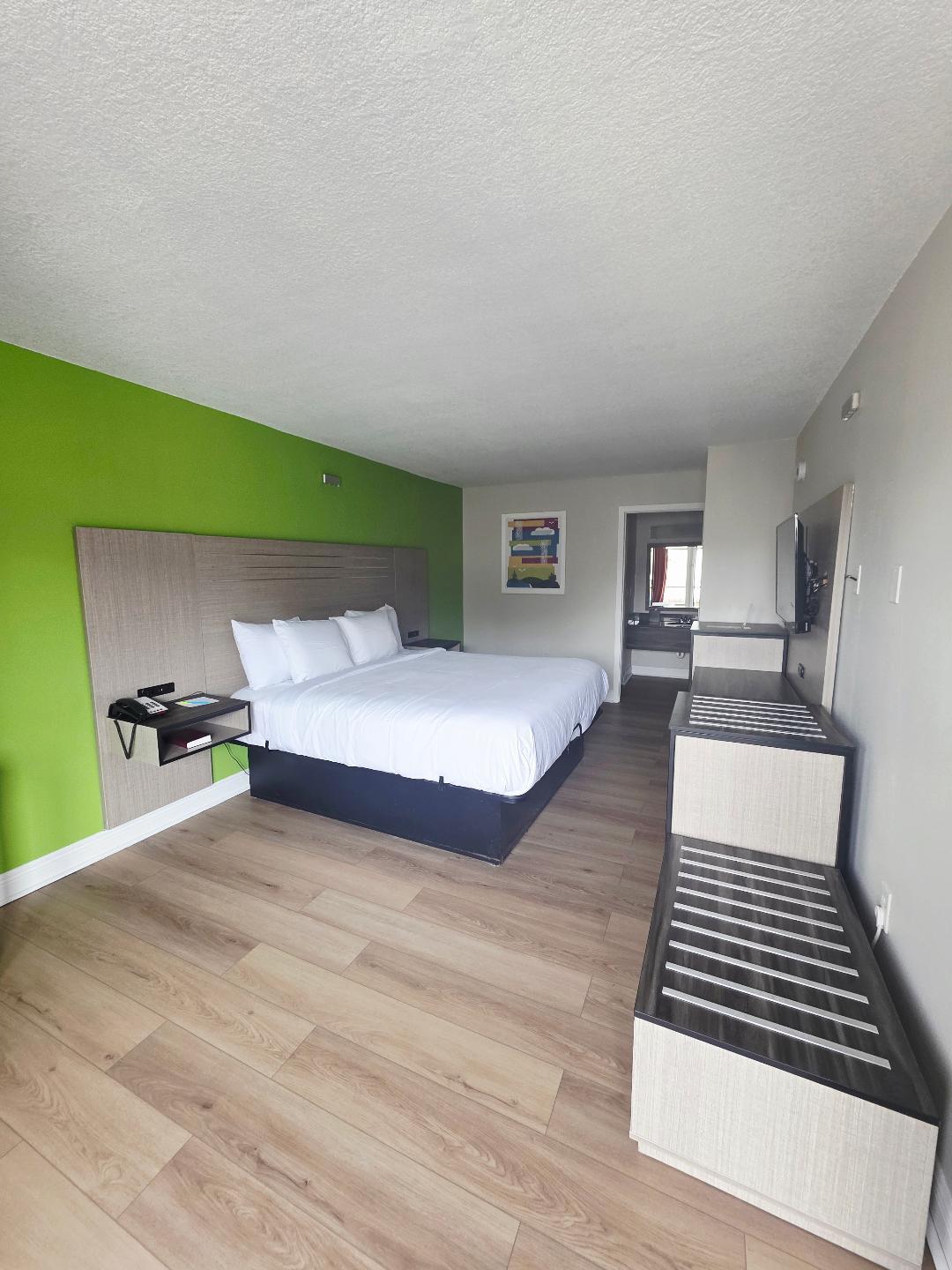 One King Non-Smoking guest room with a king bed against a green accent wall, a wall-mounted TV and an open bathroom doorway