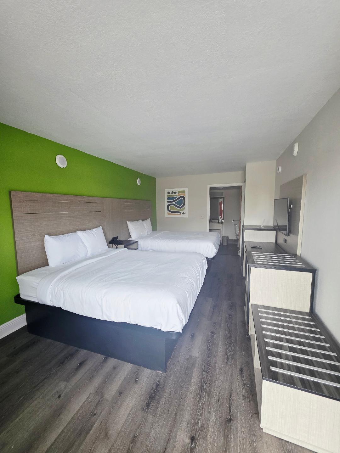 Two Queen Non-Smoking guest room with two queen beds against a green accent wall and a wall-mounted TV